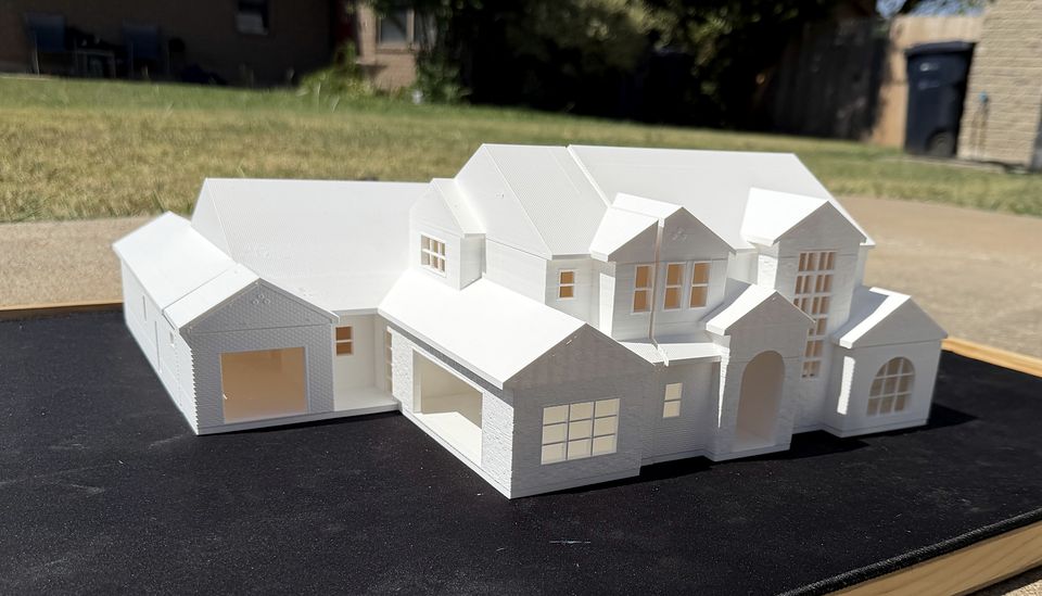 The Adeline by BR Custom Homes, a large white 3D printed two-story custom home model with the roof on, seen from the front corner, showing multiple gables, a covered entry and window grids